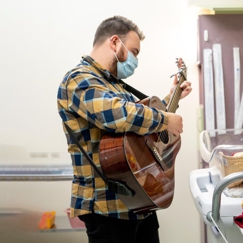 tyler reidy wearing a mask playing a guitar in a hospital 