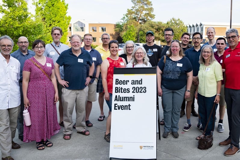 alumni gathered around a sign inscribed with the words "beer and bites 2023 alumni event"
