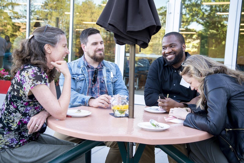 alumni sitting around a table outside with an umbrella in the table