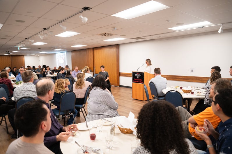 A Grebel alumni speaks at a podium at the front of the dining room