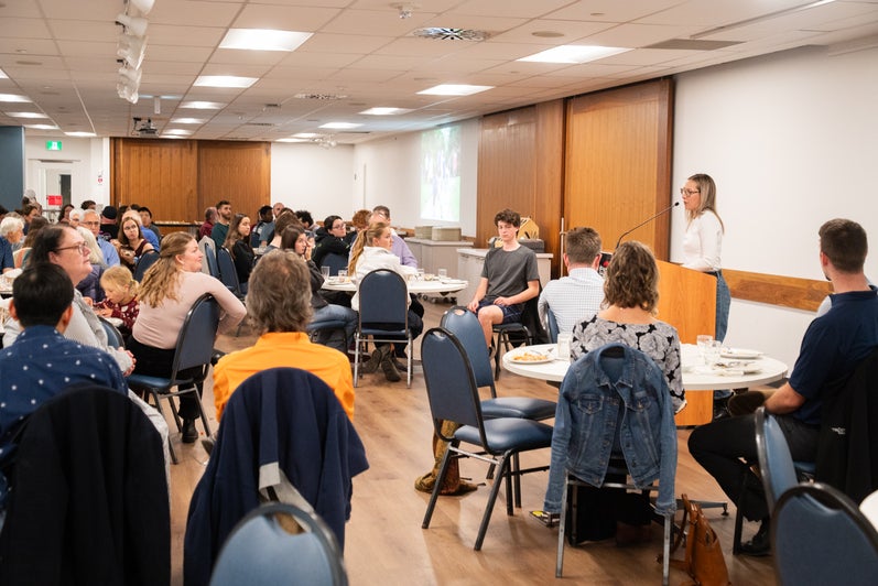 A Grebel alumni speaks at a podium at the front of the dining room