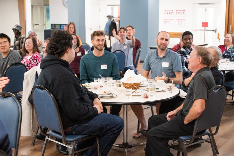 Peter Hart sits at his table with Grebel Alumni, all smiling. 
