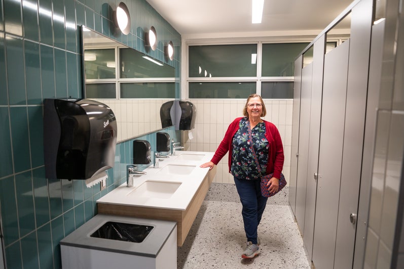 A woman stands in the new Grebel residence washroom. It's brightly lit with blue and white tile.