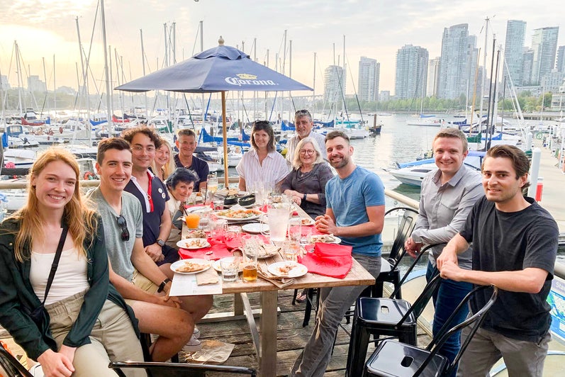 alumni around a table outside by the water