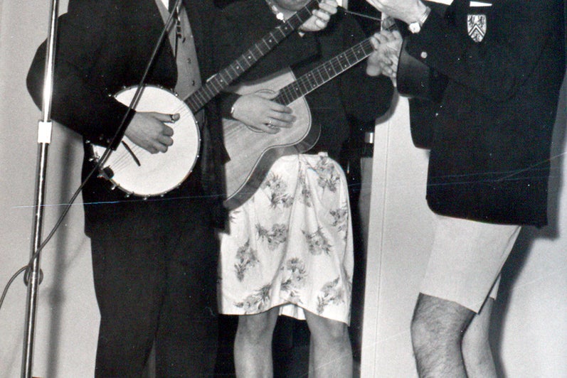 A group of students play banjoy and sing in front of a microphone (black and white photo)