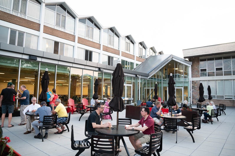 Grebel alumni sit at patio tables outside the iconic peaked rooves