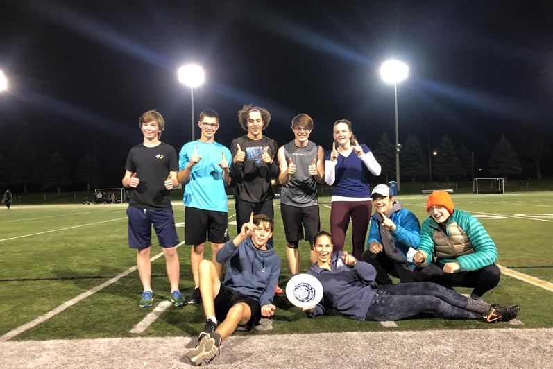 students posing with a Frisbee on a football field 