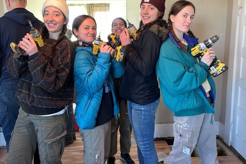 five students posing with drills while repairing a home 