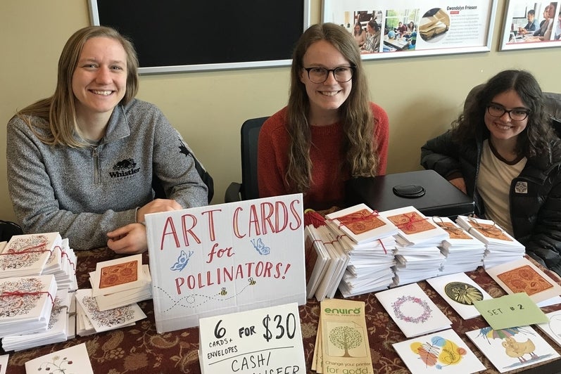 three students sitting at a table covered in cards for pollinator garden 
