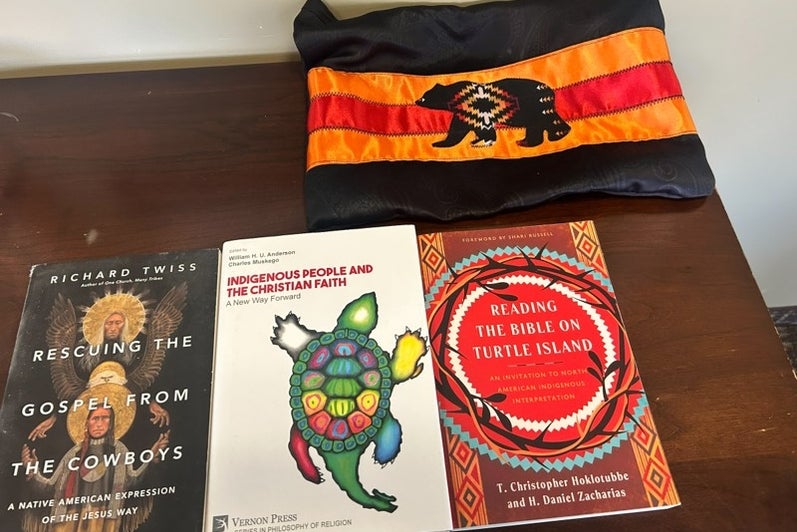 Three indigenous teachings books and a cloth with orange, red, and a black bear.