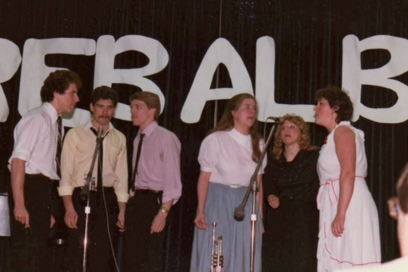 Students sing together in front of a banner in the 80s