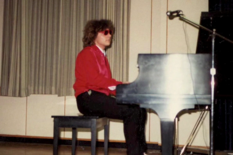 A student in a red sweater plays the piano in the great hall (80s)