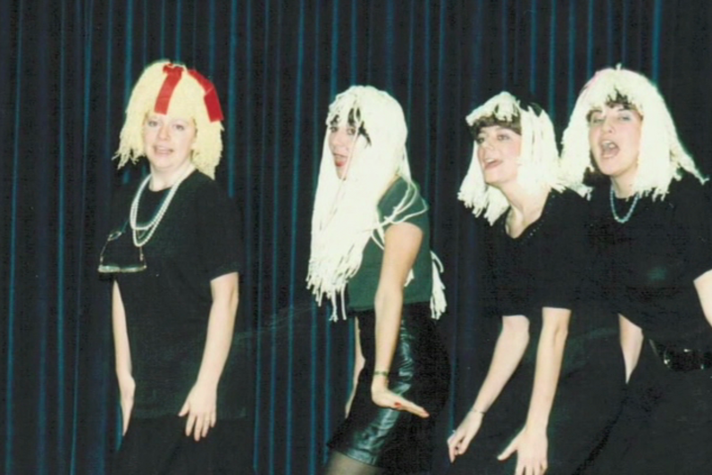 four students in white wigs and black dresses perform a skit during a talent show in the 80s