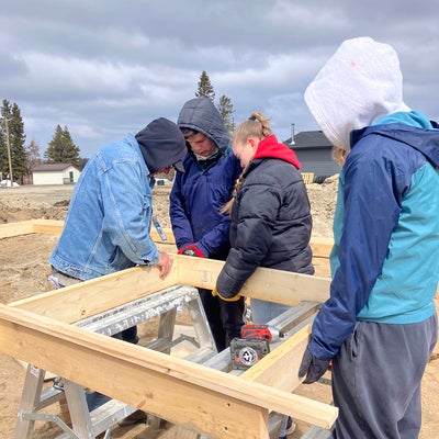 a man teaching three students how to make wooden frames for pouring cement