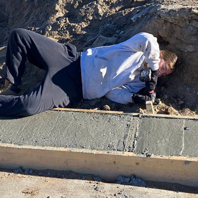 a student laying in the dirt, dismantling frames used for cement foundations