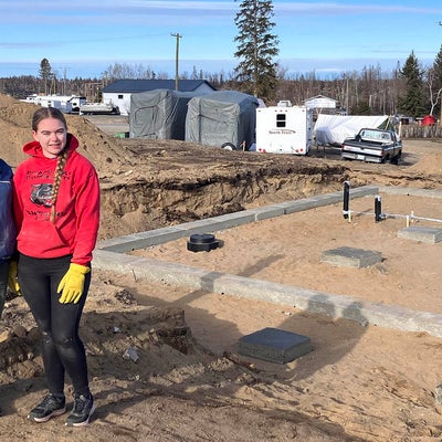 three students standing in front of the house foundation that they built