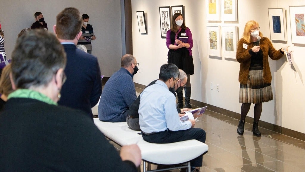 Carol pointing to an artwork in a full art gallery 