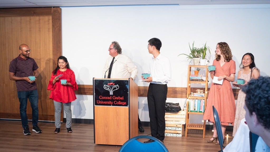 Charles and Clare standing to the left of on the Conrad Grebel Podium in the dining hall with four other people with them