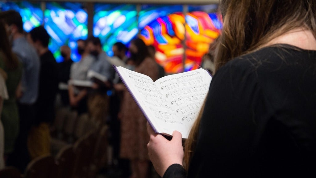 song book held by student in front of chapel window 