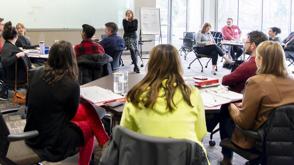 people gathered in table groups facing a speaker standing in the front of the room