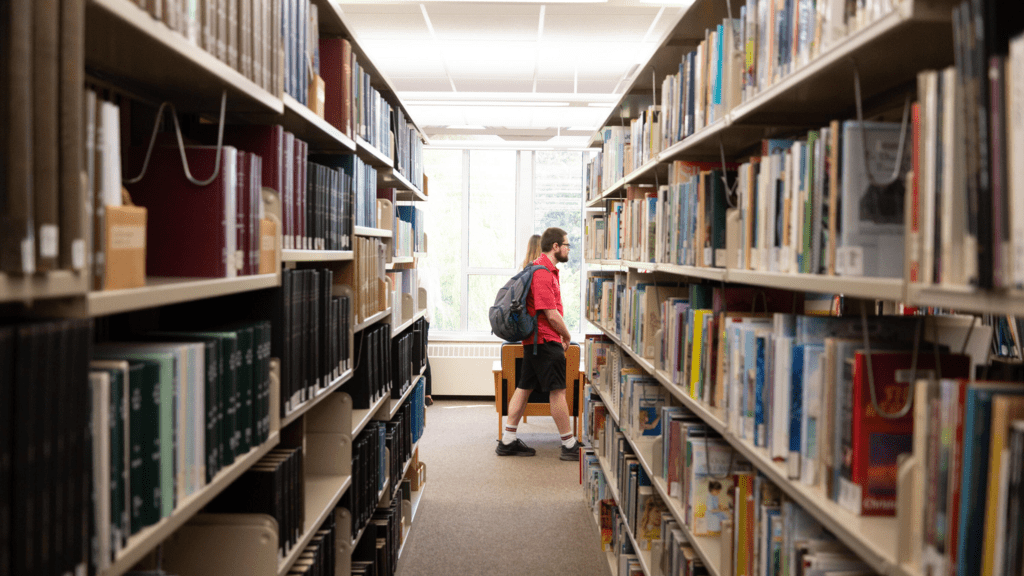 grebel students walking past library shelves 