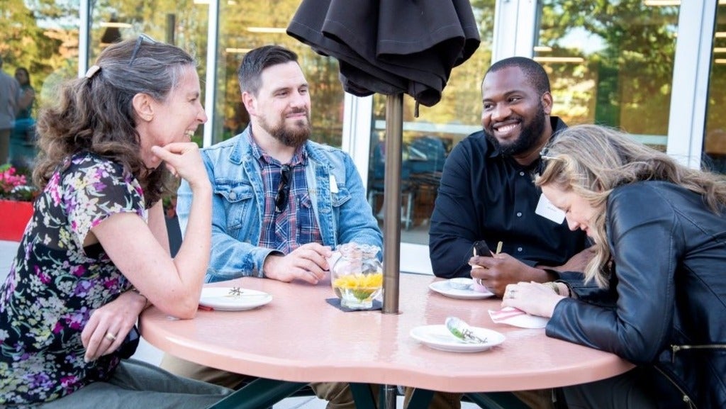 Three MTS alumni and a faculty member laugh together around a patio table