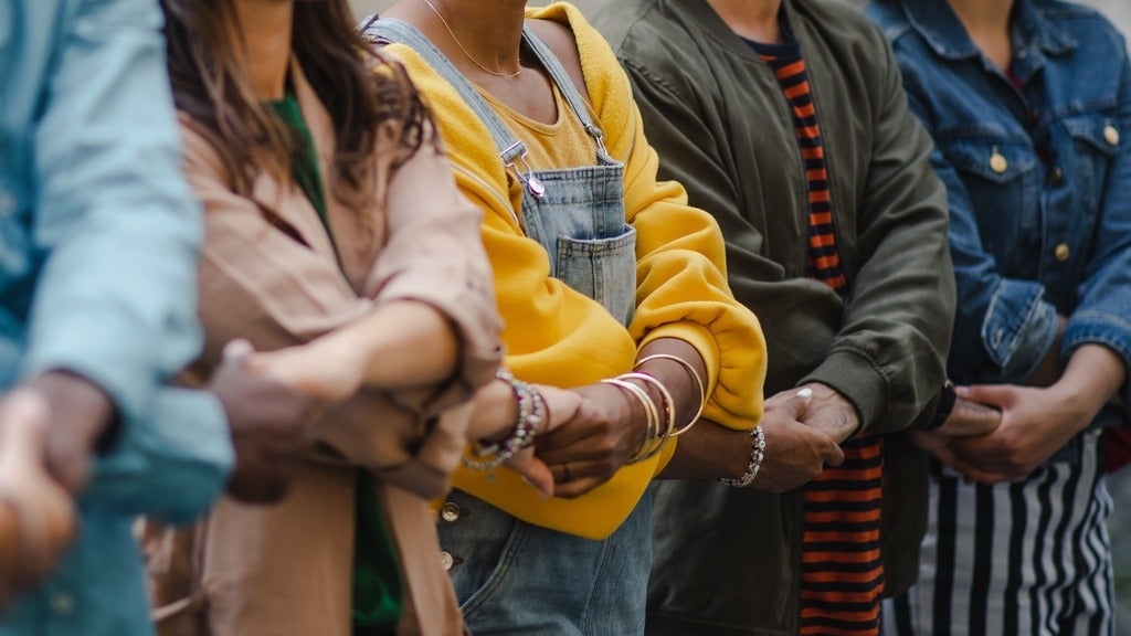 several people of ethnic backgrounds cross their arms and hold hands in a line together.