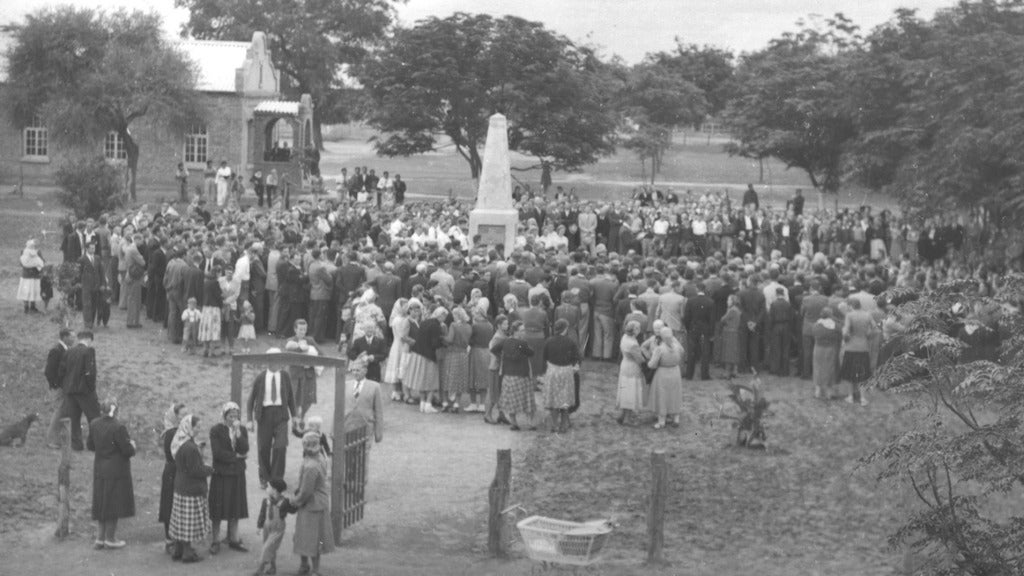 black and white photo of a crowd in an open area, sorroungind a tall white memorial stone.