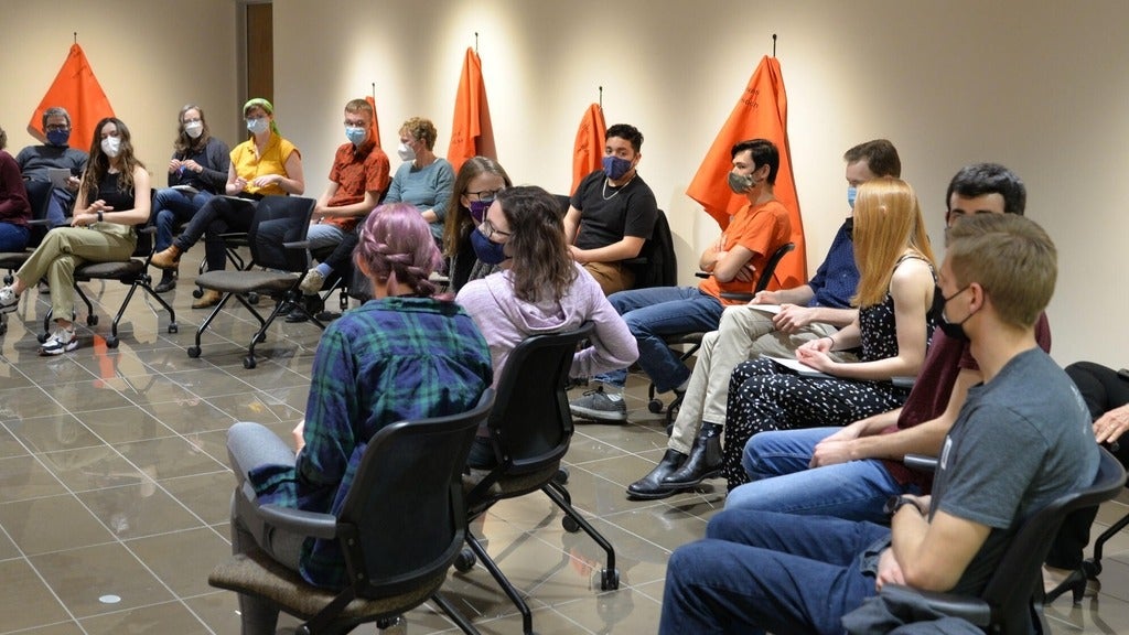 students sitting in a semi circle facing a mic 