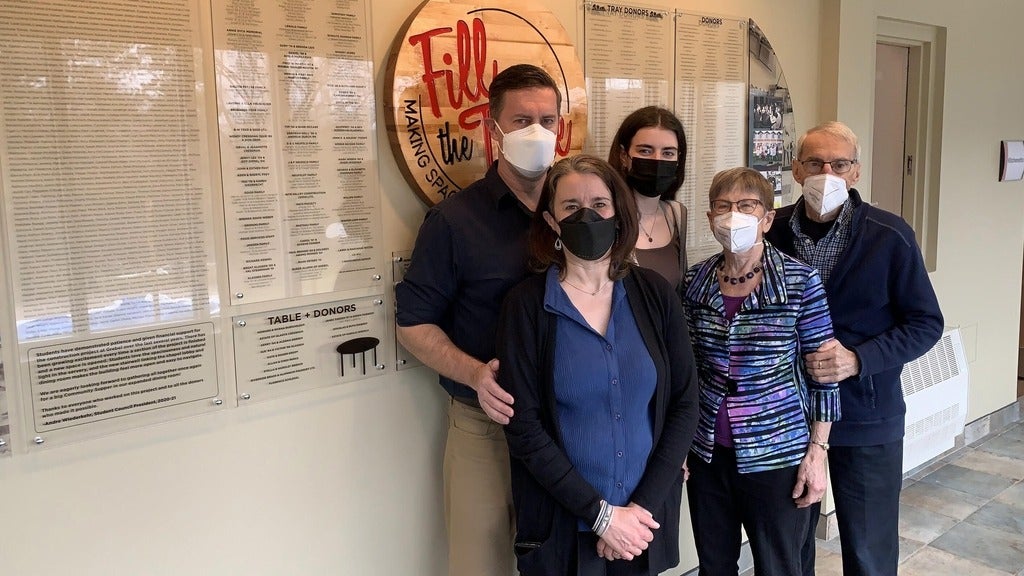 four people wearing face masks standing beside wooden sign that says "fill the table"