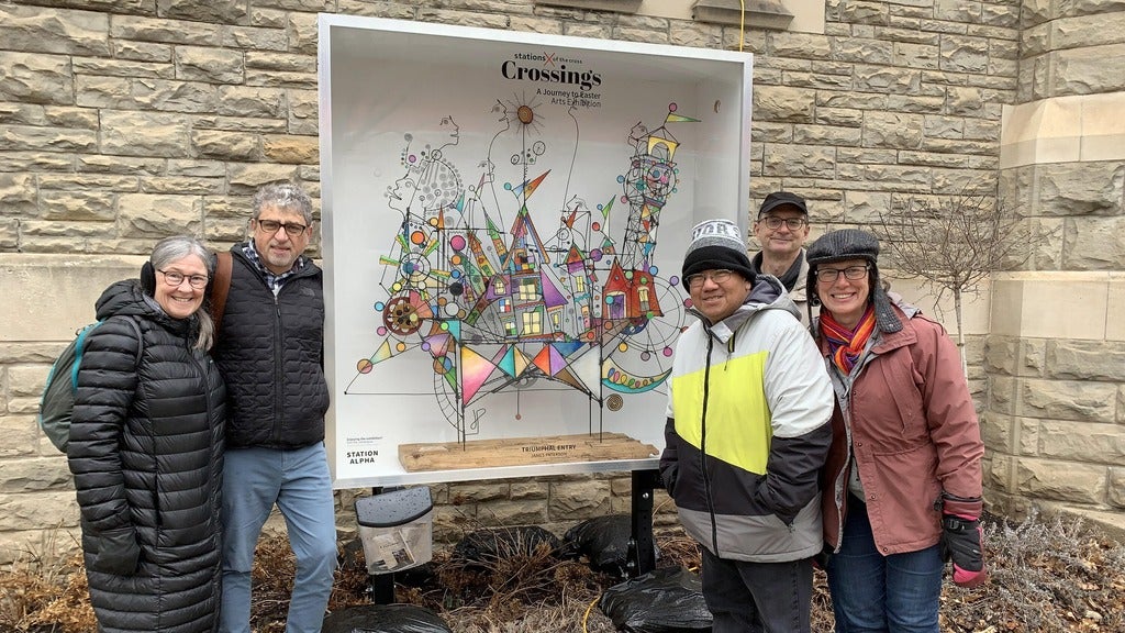 five people standing by colourful stained glass inspired wire sculpture. 