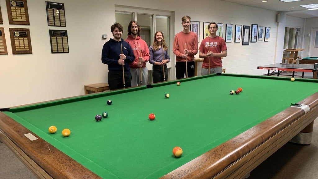 five students standing behind a poll table holding cues