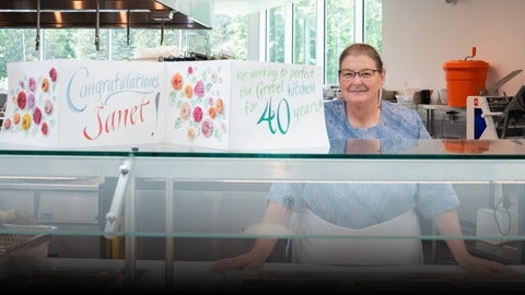 Janet Martin standing beside a giant card that celebrates 40 years of working in the kitchen