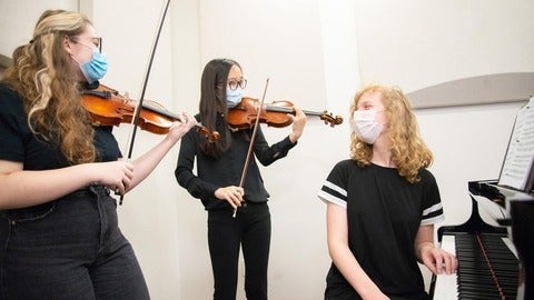 three students playing violins and piano 