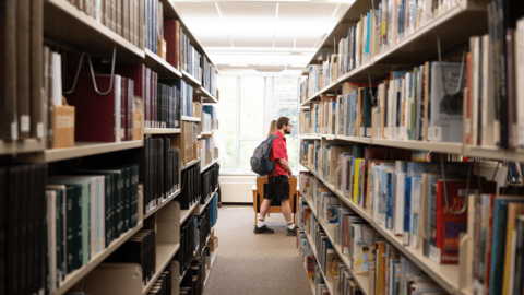 grebel students walking past library shelves 