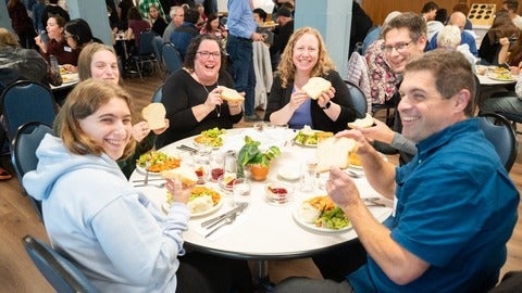 A group of Grebel students and alumni show off fresh baked bread during at the dinner table