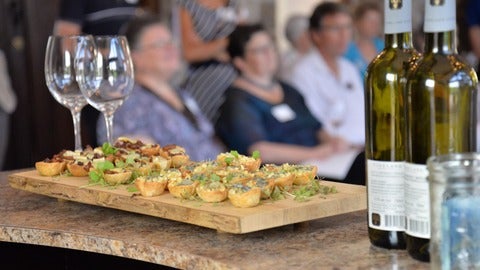 A wooden plate of snacks sits on a bar with wine glasses during a Grebel event