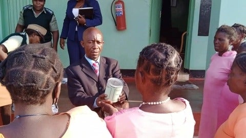 Issa holding out a can of meat to a female prisoner