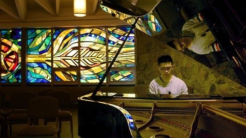 nicholas wong playing a piano in fornt of stained glass window in a chapel