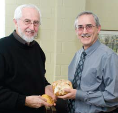 At a small Grebel celebration, Ernie Regehr stands with his Pearson Peace Medal as Henry Paetkau presents him with Grebel’s own style of medal - a massive cinnamon bun!