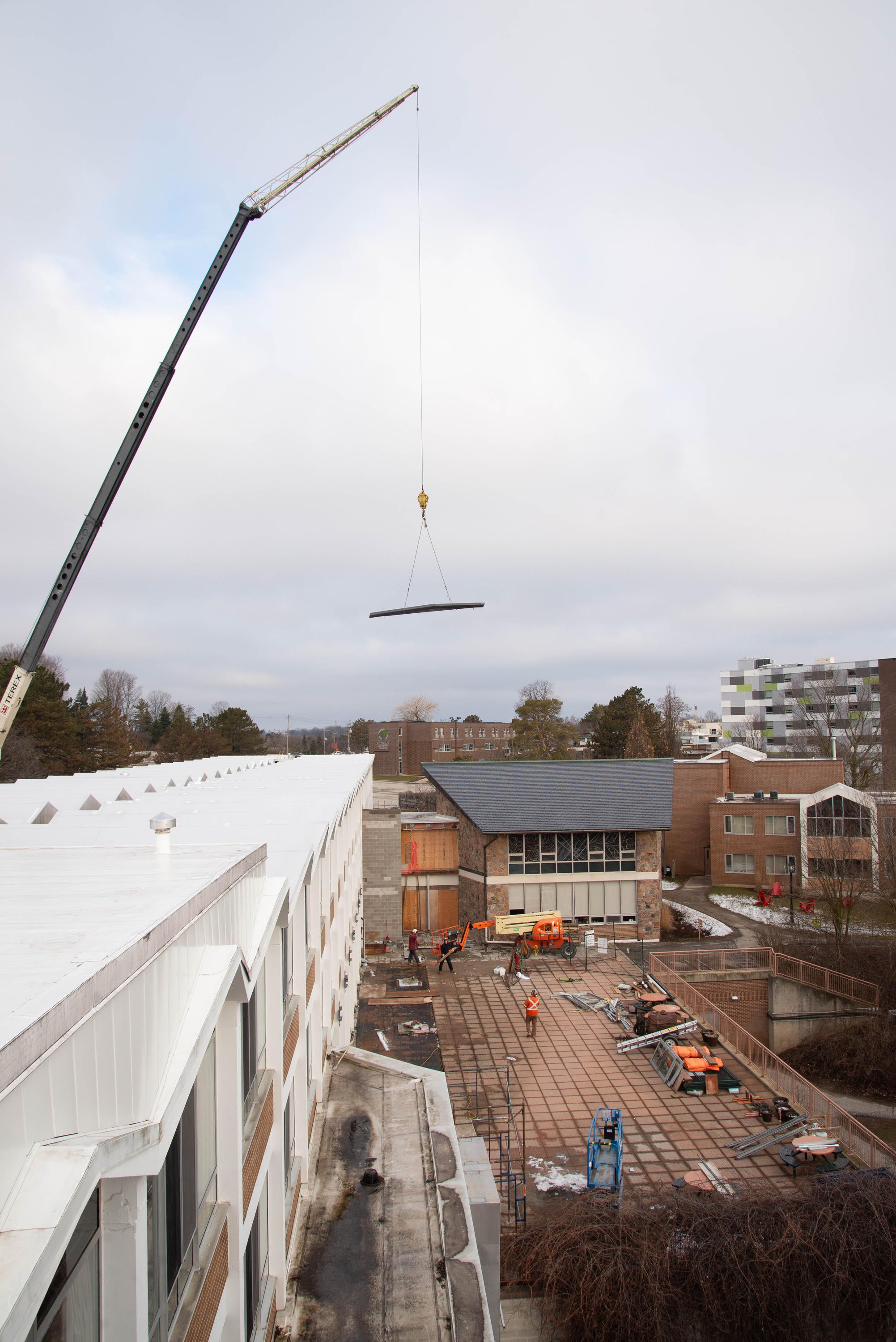 A crane towers over the residence building, carrying steal beams to the patio