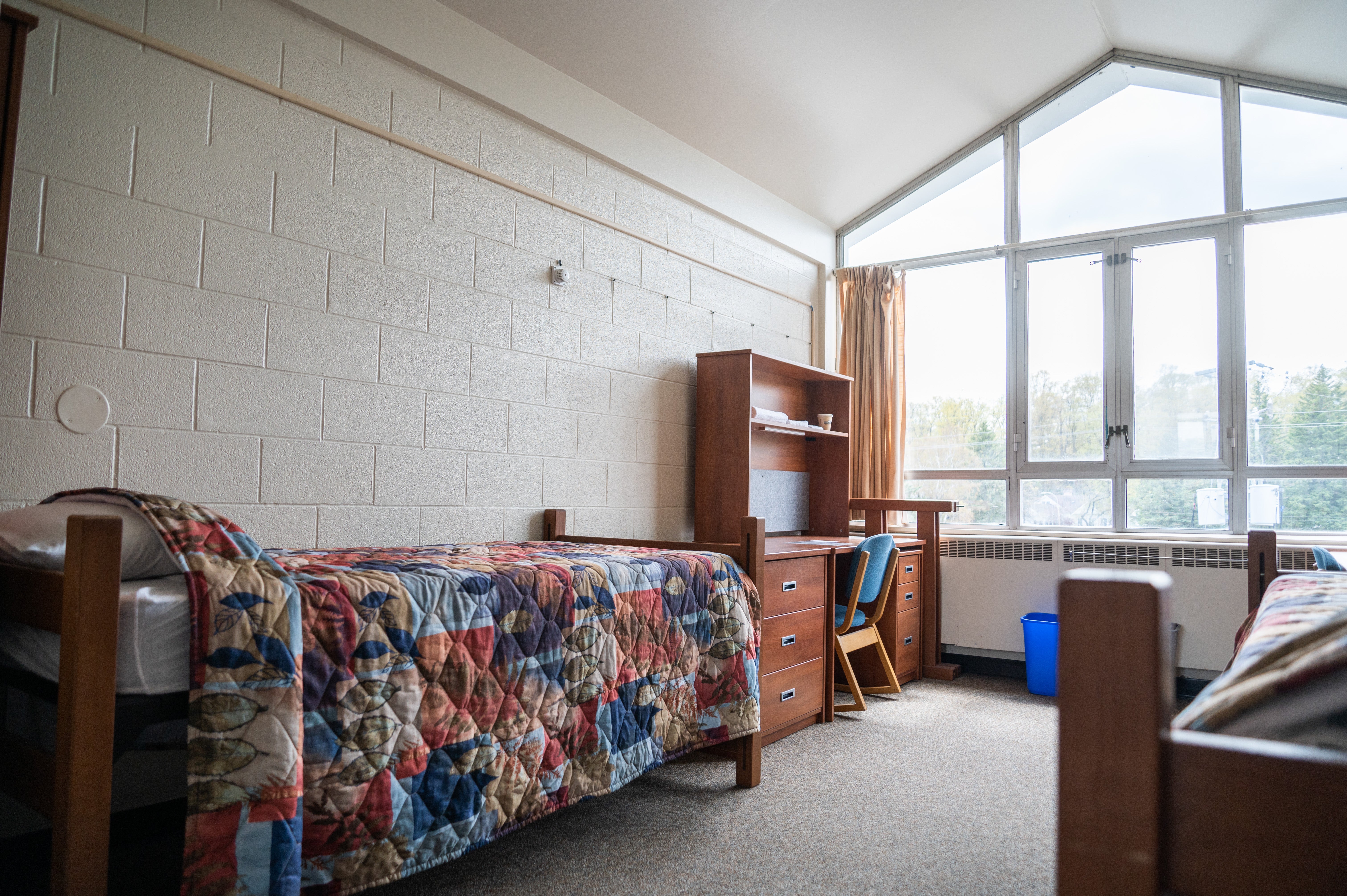 a room with a bed, desk, and a large window