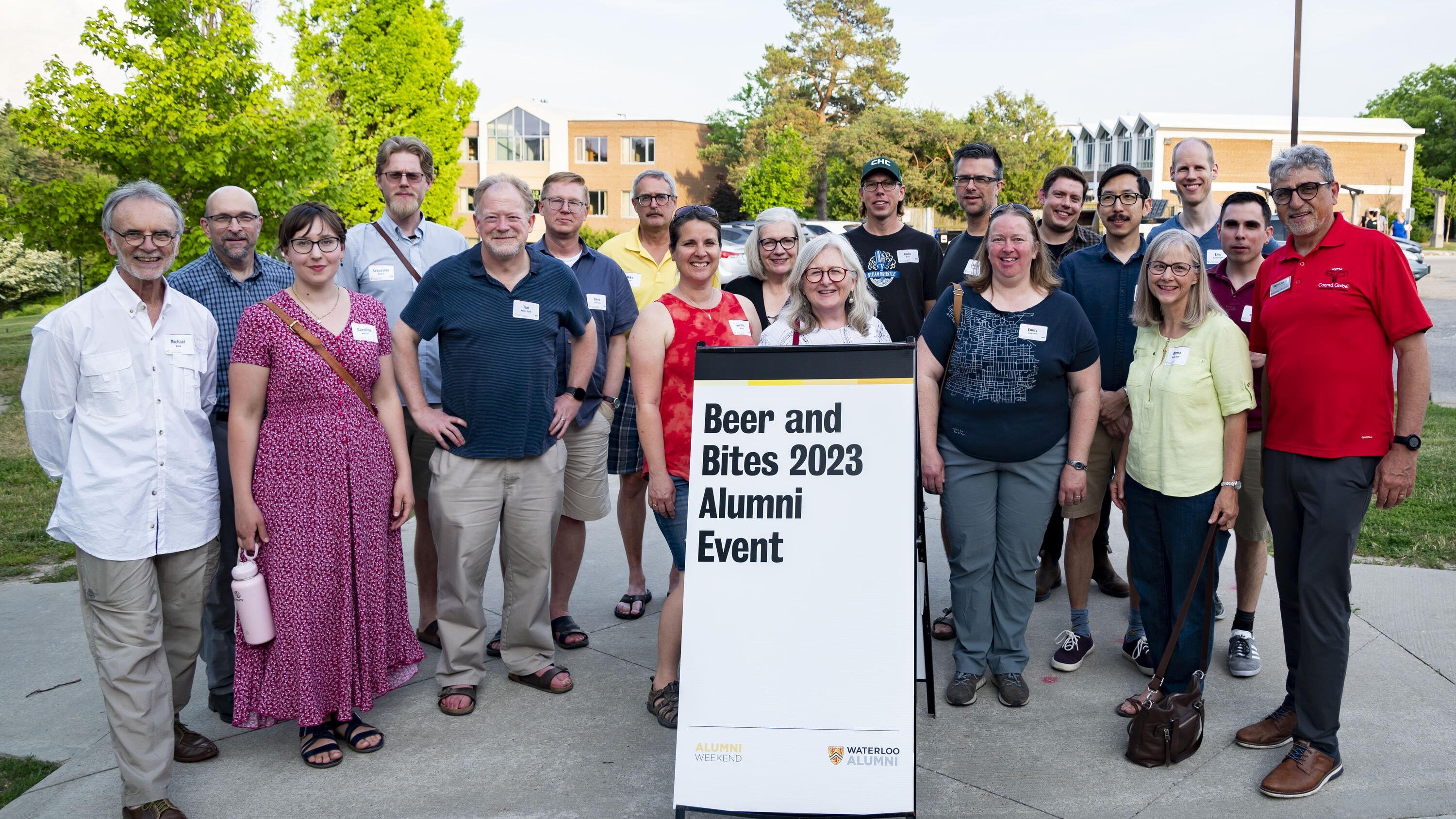 alumni gathered around a sign inscribed with the words "beer and bites 2023 alumni event"