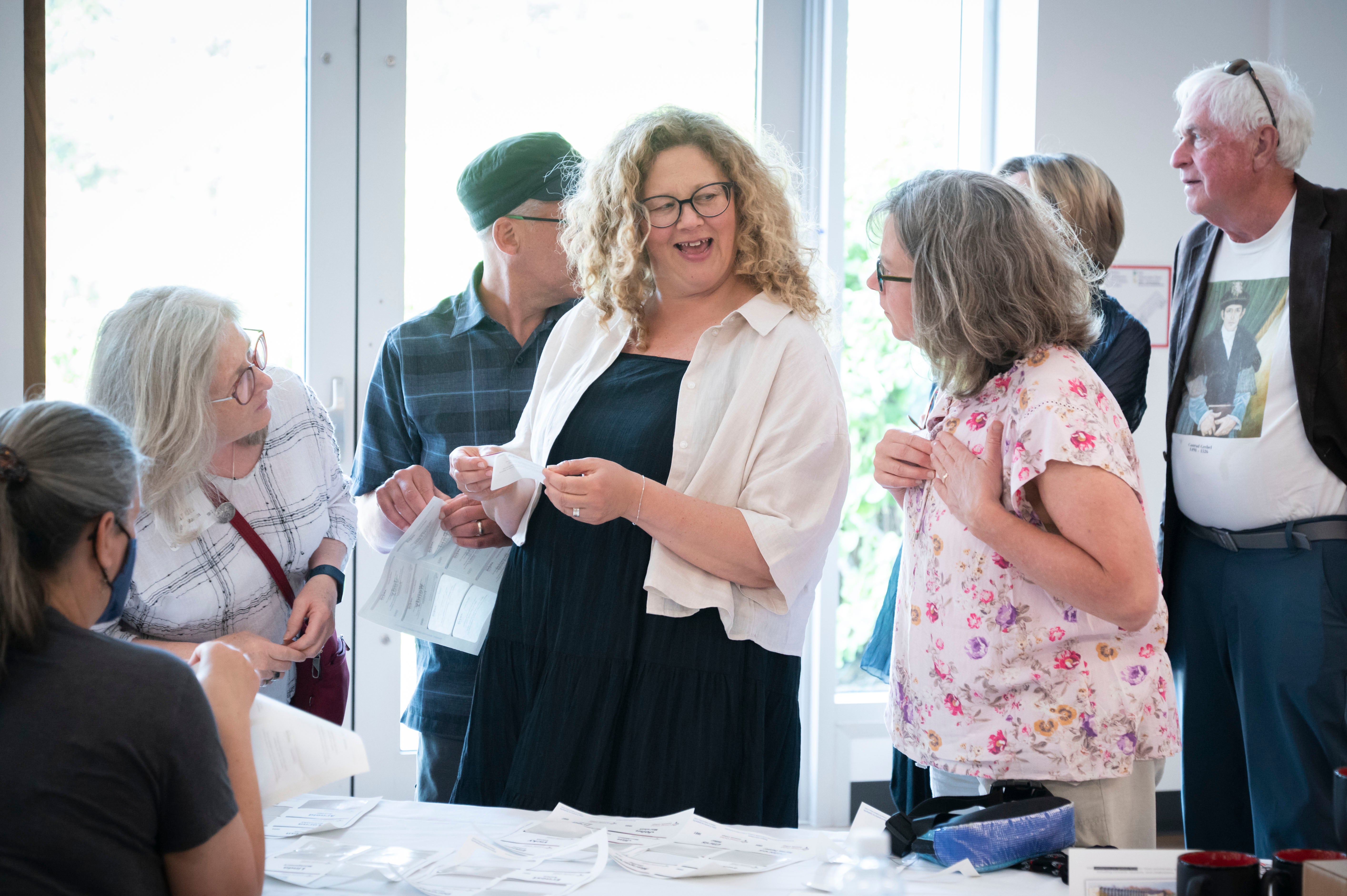 Two woman, Grebel Alumni, laugh as they put on their nametags at the registration table