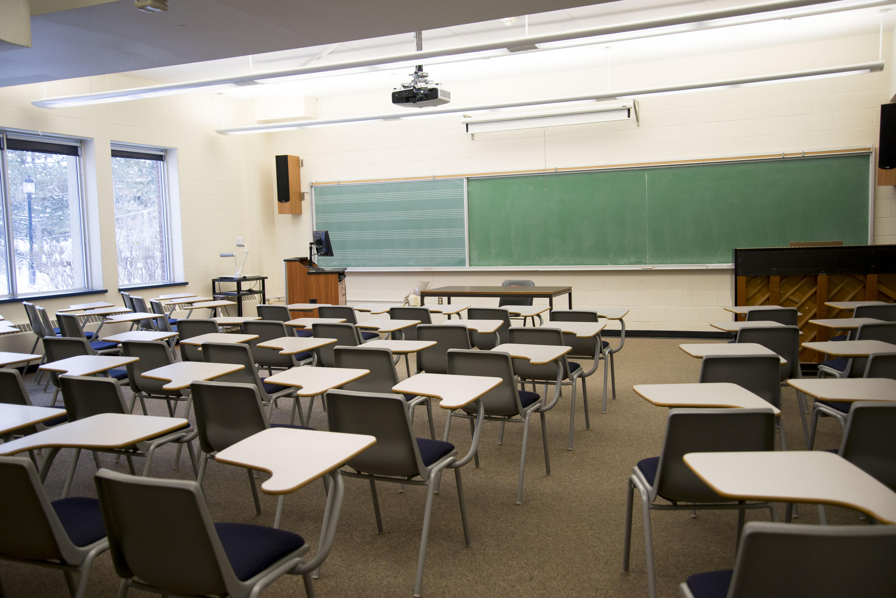 Classroom with individual chair desks, a chalkboard, a projector, and an upright piano