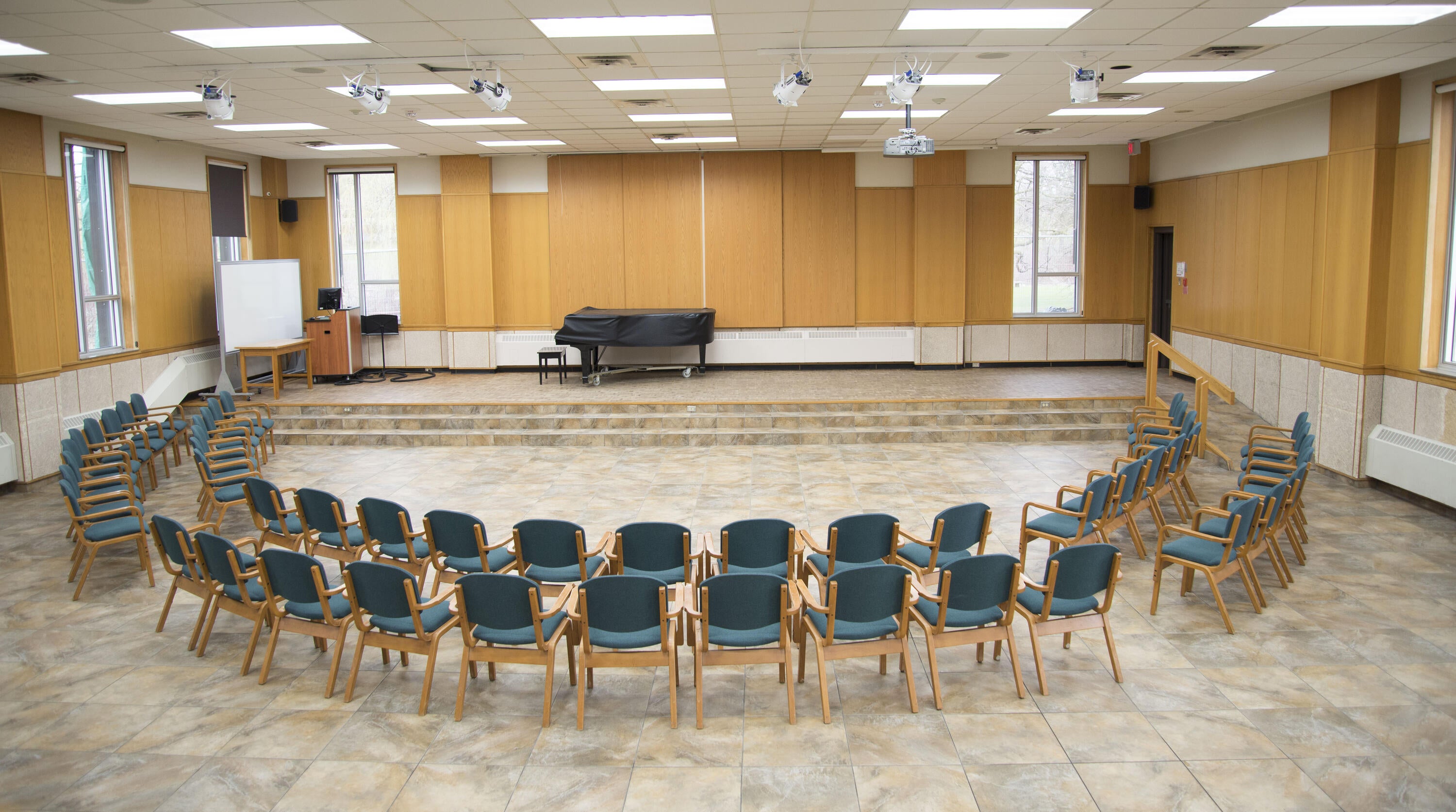 Large hall with tables, chairs, a projector, and a grand piano