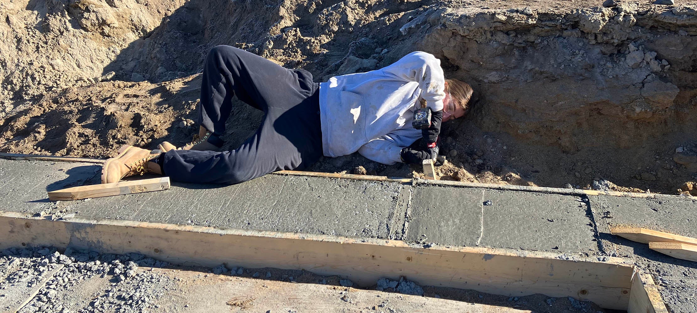 a student laying in the dirt, dismantling frames used for cement foundations