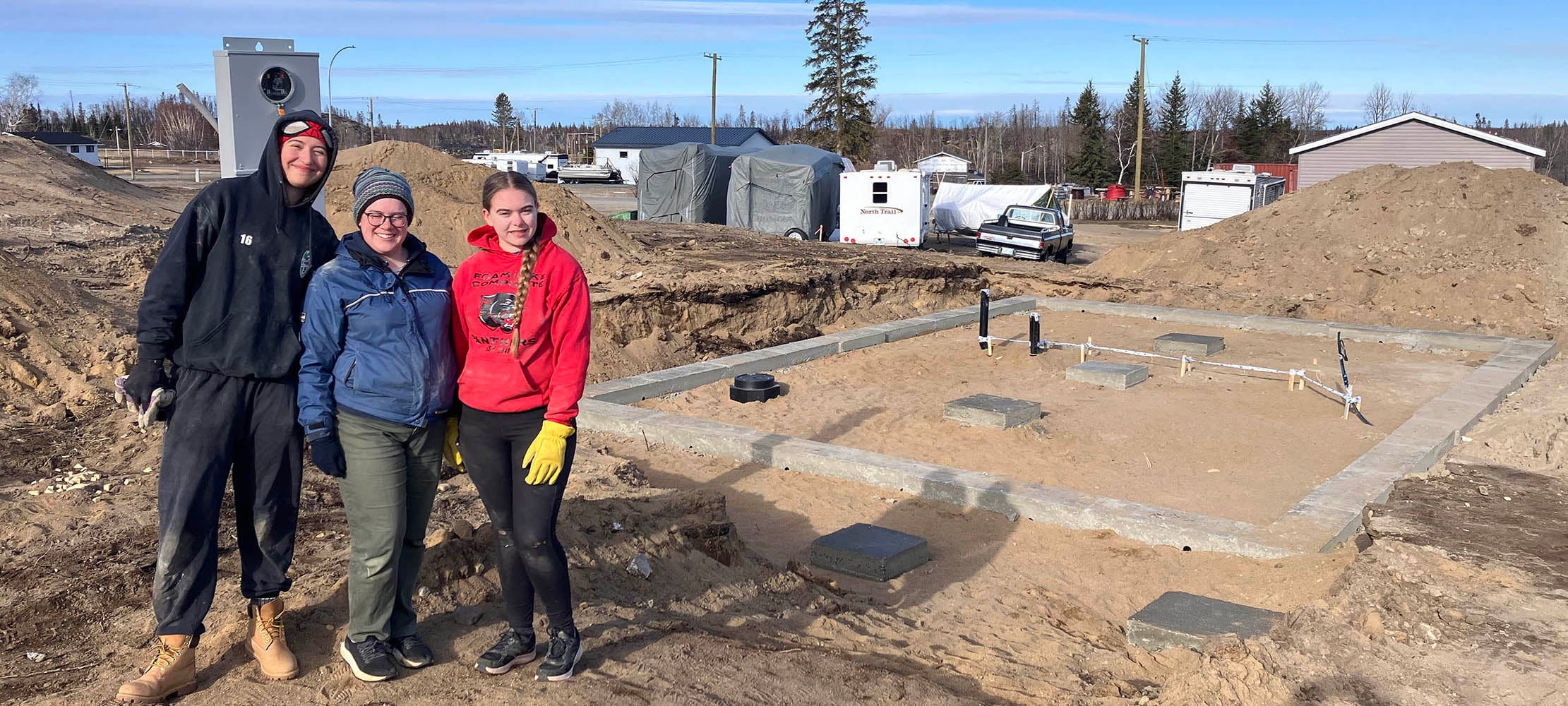 three students standing in front of the house foundation that they built
