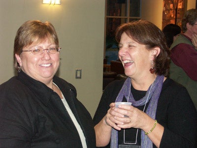 Two women talking, one is holding a coffee cup and laughing at what the other woman is saying.