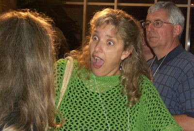 A woman in a green poncho who is very excited to see someone she knows